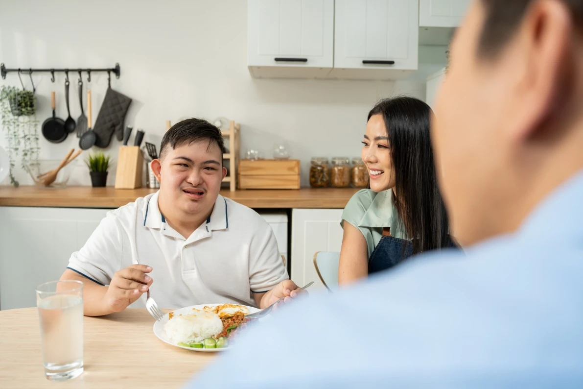 Disabled man with down syndrome eating meal at kitchen bench with parents